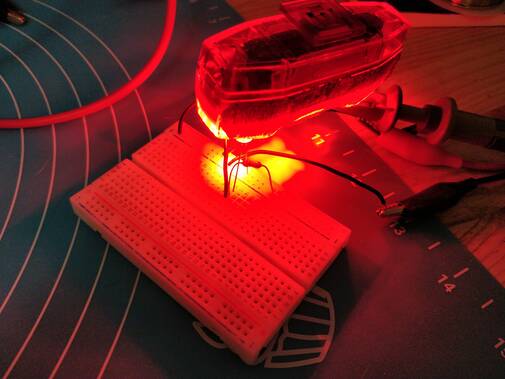 Photo of the circuit on a breadboard, with an oscilloscope probe connected to V_out and a bright red bike light resting on top.