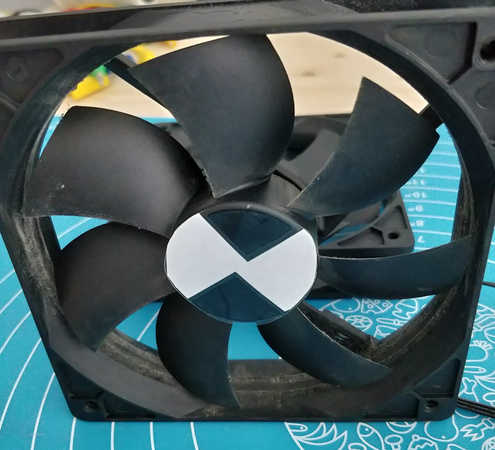 PC fan with a circular piece of paper taped to the center section. Two 45° notches are cut out of the circle opposite each other.